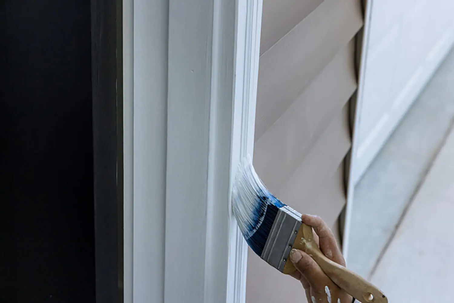 Painter applying exterior paint to trim, illustrating the best time to paint the exterior of a house for proper adhesion and finish