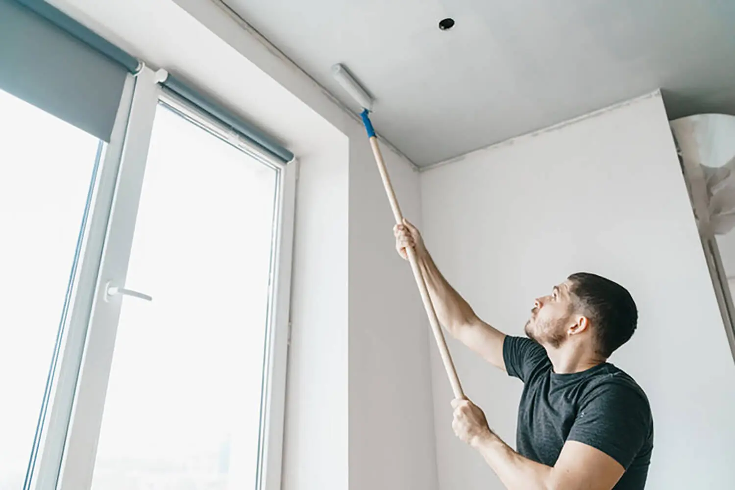 Man repainting interior ceiling near window, showing signs it may be time to repaint your home’s interior